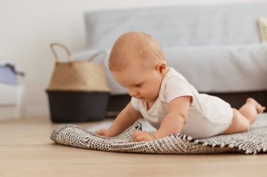 Beyaz elbiseli, beyaz elbiseli, tatlı bir kızın yan görünüm portresi oturma odasında yerde yatıyor, arka planda gri kanepe var, dünyayı inceliyor..