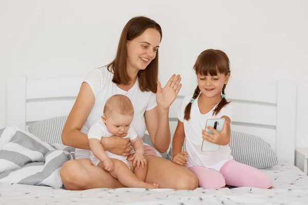Beyaz Tişörtlü Bir Anne Iki Kız Yatakta Oturmuş Akıllı Telefon — Stok fotoğraf