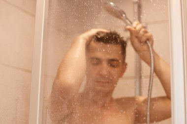 Sakin, esmer, genç, yakışıklı, duş alan, suyun altında çıplak poz veren, yoğun çalışma gününden sonra dinlenen, ferahlatıcı bir adam..