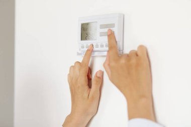 Bilinmeyen kadın, evdeki akıllı dokunmatik ekran ai teknolojisi ile bağlantılı cihazları kullanarak evdeki enerji güvenliği ısıtma sistemi dijital kontrolünde duvara takıyor..