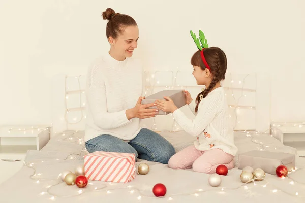笑顔の母と娘身に着けていますカジュアルスタイルの白いセーター上に座っています 女性与えますプレゼントボックスへ彼女の子供 お祝いの女の子とクリスマスと新年 — ストック写真