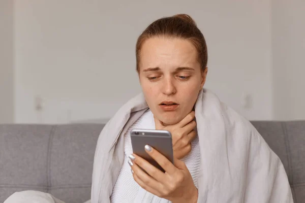手拿着手机 手拿着毛圈 坐在沙发上 手拿着毛圈 喉头酸痛 拨打医生电话 流感症状的女性形象 — 图库照片