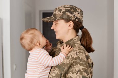 Yüzünde kamuflaj üniforması ve şapkası olan gülümseyen askeri annenin, çocuğuyla karşılaştığında sevgisini ve neşesini ifade eden, savaştan ya da ordudan sonra evine dönen,.