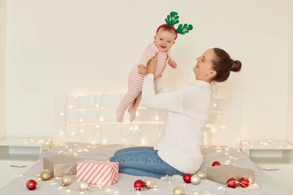 幸せな興奮した女性ですお祭り気分投げ彼女の幼児娘で空気中 幼児の女の子はストライプベッドと鹿のフープを着て クリスマスと大晦日を祝います — ストック写真