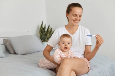 Elinde at kuyruğu, elinde gebelik testi olan çekici bir kadının yatağında küçük kızıyla oturduğu poziyonlar. Olumlu sonuçlara bakıp mutluluk ve neşe ifade ediyor..