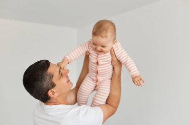 Küçük kızıyla evde oynarken gülümseyen yetişkin bir babanın portresi çizgili küçük kızını kaldırıyor, birlikte vakit geçirmekten keyif alıyor..