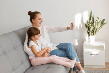 Gülen anne ve kızın selfie çekmesi ya da oturma odasında video görüşmesi yapması, koltukta oturup cep telefonu kamerasına bakması..