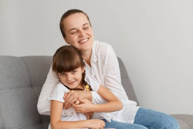 Çok mutlu bir annenin portresi. Koyu saçlı tatlı kızına sarılıyor. Kadın gözlerini kapatıyor..