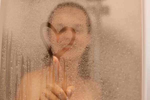 Photo Smiling Attractive Young Woman Draws Heart Weeping Glass Shower — 스톡 사진