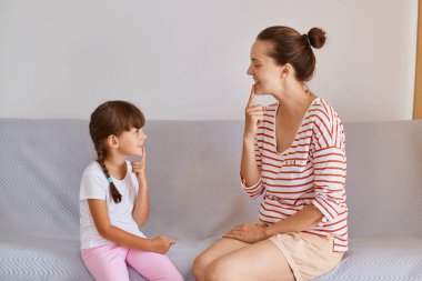 Sesleri ve dil sorunlarını iyileştirmek için ders alan kadın ve küçük kız portresi, rahat koltukta oturan ve konuşma alıştırması yapan kadın çocuk..