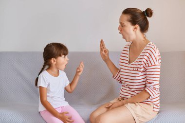 Küçük bir kızla evde çalışan öğretmen kanepeye oturmuş, küçük bir çocuk dil dersi alıyor, seslerin telaffuzunu ve telaffuzunu öğreniyor..