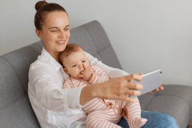 Mutlu, iyimser bir kadının portresi küçük kızıyla koltukta oturup selfie çekerken ya da görüntülü konuşma yaparken pozitif duyguları ifade ederken..