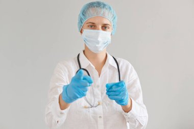 Tıbbi başlık, eldiven, ameliyat maskesi ve cübbesi takan, ayakta durup kameraya bakan ve seni tıbbi muayene için seçen kendine güvenen bir doktor kadının kapalı çekimleri..