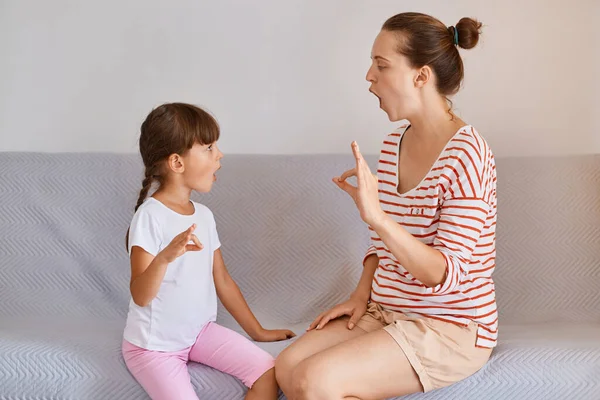 女性理学療法士の屋内ショットは ソファに座っている間に屋内で小さな子供の女の子とポーズ スピーチの問題を修正 音を発音する方法を示しています — ストック写真
