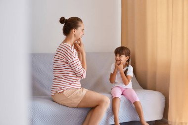 Çalışkan bir kadın konuşma terapistinin portresi, küçük bir kızdan ders alması, günlük kıyafet giyen insanlar, pencerenin yanındaki koltukta oturup konuşmayı öğrenmeleri,.
