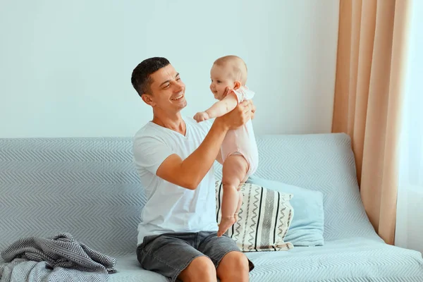 Koyu renk saçlı, beyaz tişörtlü, kotlu yakışıklı bir baba. Pencerenin yanında öksürüp bebek kucağında oturuyor. Çocukla vakit geçiriyor, gülüyor..