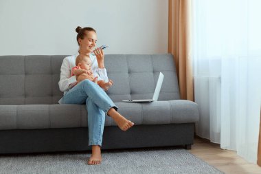 Beyaz gömlek ve kot pantolon giyen mutlu bir kadının portresi bebek kızıyla koltukta oturuyor, bilgisayarla uğraşırken arkadaşına sesli mesaj kaydediyor ve çocukla vakit geçiriyor..