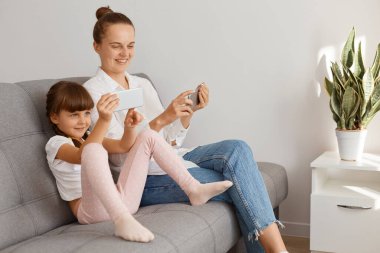 Beyaz gömlekli ve kotlu bir kadının çocuğuyla aynı koltukta oturduğu, insanların telefon kullandığı, annenin görüntülü konuşma yaptığı, iyimserliğini ifade ettiği kapalı bir çekim..