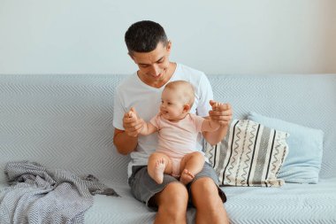 Beyaz t-shirt ve kot pantolon giyen çekici esmer adamın portresi öksürük ve kucağında bebek, büyüleyici bir gülümsemeyle kızına bakıyor ve sevgisini ifade ediyor..