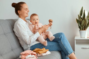 Küçük kızıyla öksürürken, beyaz gömlek ve kot pantolon giyen bir kadının çocuğa tahta oyuncağını gösteren çekici bir annenin yatay görüntüsü..