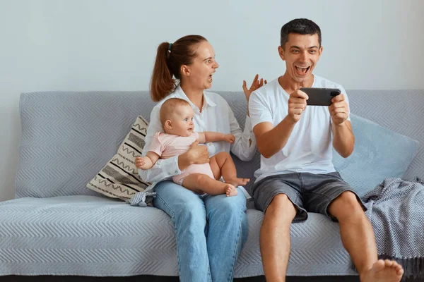 Excited Amazed Couple Infant Child Sitting Sofa Living Room Expressing — Stock Photo, Image