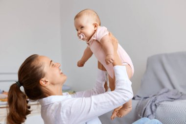 Tatmin olmuş mutlu anne portresi, siyah saçlı genç bir kadın küçük kızıyla evde oynuyor, anne kusuyor, birlikte eğleniyor..