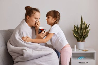 Sağlıksız bir kadının çay içerken, burnu akarken, tatlı bir çocuğun hasta annesine sarılırken, annesine bakarken, evde ışık odasında poz verirken..