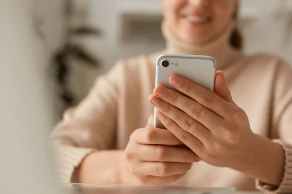 穿着米色休闲装 用手机 在社交网络上观看视频或输入电子邮件 表达积极情感 微笑的女性的特写 — 图库照片