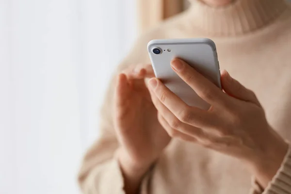 携帯電話をオンライン通信に使用して 手に携帯電話を保持ベージュのカジュアルなスタイルのセーターを身に着けている匿名の女性のクローズアップ肖像画 メッセージを入力 — ストック写真