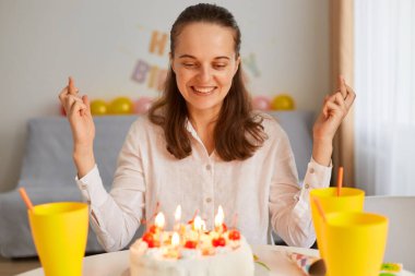 Son derece mutlu koyu renk saçlı bir kadının doğum gününü kutlaması, pastaya bakması, dua etmesi, dilek tutması, mum üflemeye hazır olması, mutluluğu ifade etmesi..