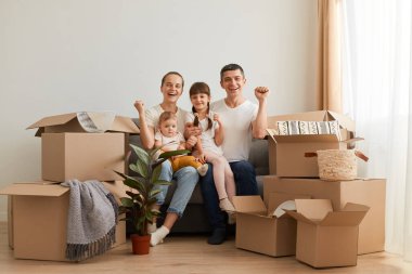 Taşındıktan sonra çocuklarla aynı koltukta oturan, kollarını kaldıran, olumlu duygularını ifade eden, yeni bir ev satın almayı veya kiralamayı kutlayan heyecanlı aile portresi..