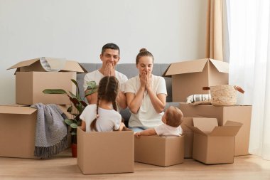 Mutlu, heyecanlı bir ailenin portresi, çocuklarla birlikte yerde oturan heyecanlı bir yüz ifadesi, karton kutulardaki çocuklar, yeni bir eve taşınıyorlar..