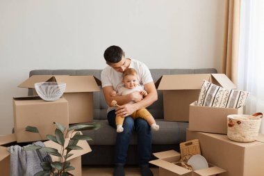 Beyaz günlük tişört ve kot giyen, küçük kızıyla koltukta oturan, taşındıktan sonra kutuları boşaltan, yeni yürümeye başlayan çocukla zaman geçiren, onu öpen yakışıklı esmer adamın kapalı çekimleri..