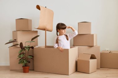 İyimser küçük bir kızın taşınma sırasında bayrakla gemi yapması ve yeni dairede denizcilik oynaması, taşınırken eğlenmesi, eşyalarla çevrili paketlerle poz vermesi..