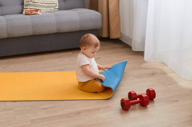 Bir çocuğun yoga minderinde halterlerle otururken, aydınlık odada tek başına oynarken, kelime çalışırken, tuhaf bir ifadeyle bakarken, spor minderini keşfederken..