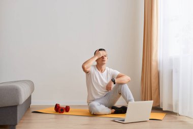 Genç fitness adamının portresi hayal kırıklığına uğramış, çaresiz, kızgın ve üzgün, elleri başında, evde spor yaptıktan sonra ya da spor yaparken baş ağrısı çekiyor..