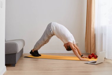 Genç, beyaz bir adamın portresi yoga yapıyor, aşağı doğru köpek egzersizi yapıyor, adho mukha svanasana pozu, spor kıyafetleri giyiyor,.