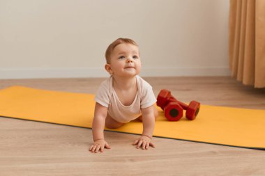 Kapalı alanda yoga minderinde yürüyen, spor malzemelerinin yanında oynayan, kelime çalışkan, yukarı bakan, yalnız poz veren bir çocuk fotoğrafı..