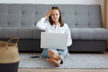 Koyu renk saçlı bir kız öğrencinin evinin zemininde dizüstü bilgisayarla oturup ders çalışırken, hata yaparken, ellerini başının üstünde tutarken, olumsuz duygular ifade ederken..