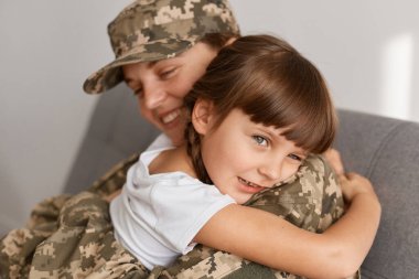 İyimser genç asker kadın kamuflaj üniforması ve şapkası giyiyor, ordudan eve dönüyor, çocuğuyla oturuyor ve ona sarılıyor, annesini kucaklıyor, çok şey kaçırıyor..