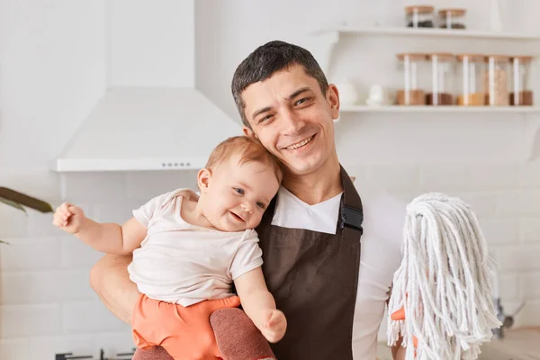 Uśmiechnięty Optymista Białej Koszuli Brązowym Fartuchu Stojący Kuchni Córeczką Mopem — Zdjęcie stockowe