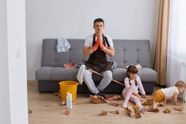 Rahat bir adamın portresi günlük giysiler ve önlük giymiş, çocuklarıyla koltukta poz veriyor, sakinleşmek için yoga yapıyor, ev işi yapıyor, karısına yardım ediyor..