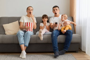 Şok olmuş aile portresi. Kanepede oturup televizyon ya da korku filmi seyrediyor. Şok ve şaşkınlığı ifade ediyor, günlük kıyafetler giyiyor, patlamış mısır yiyor..