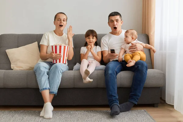 Oturma odasındaki kanepede oturan ve şok edici televizyon ya da korku filmi izleyen, şoku ifade eden, ağızlarını açık tutan, etkilenmiş çiftin kapalı çekimleri..