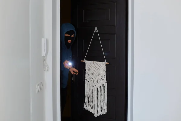 Picture of dangerous burglar breaking into house, wants to steal belongings and money, opening door and shining a flashlight to see if someone in it, breaking someone else\'s house.