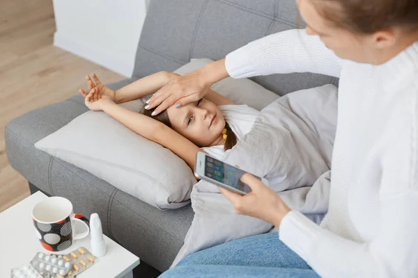 Portrait Woman Sitting Sofa Sick Daughter Keeping Hand Her Forehead — Stock Photo, Image