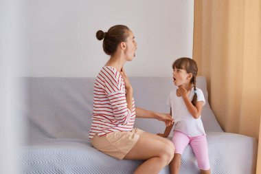 Çizgili tişörtlü profesyonel kadın konuşma terapistinin küçük bir kızla koltukta oturması, engelli çocuklara ders vermesi, sesli telaffuz ve konuşma alıştırması yapması..