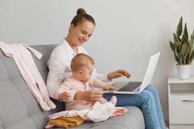 Beyaz gömlek ve kot pantolon giyen, küçük kızıyla koltukta oturan, defter üzerinde çalışan, çocuğa gülümseyen, annelik izni alan ve internetteki işine gülümseyen siyah saçlı bir kadın..