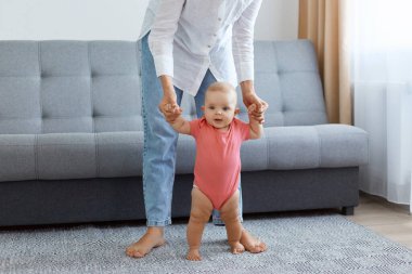 Beyaz gömlek ve kot pantolon giyen, küçük kızına gitmeyi öğreten, pencereli halıya basan ve arka planda gri kanepe olan meçhul kadının portresi.