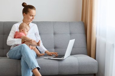 Beyaz gömlek ve kot pantolon giyen, bembeyaz saçlı, serbest çalışan genç bir kadının portresi. Kanepede oturup kızıyla vakit geçirirken internette çalışıyor..